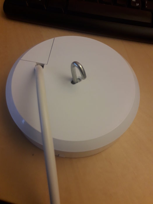 Vitt takfäste för lampa med utstickande lampsladd och monteringskrok, nära tangentbord på skrivbord.