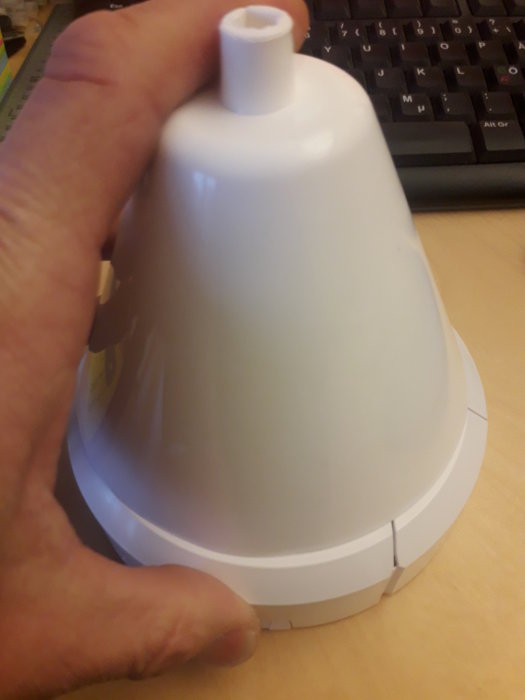 Hand håller en vit lampskärm med begränsat utrymme för anslutning, nära ett tangentbord.