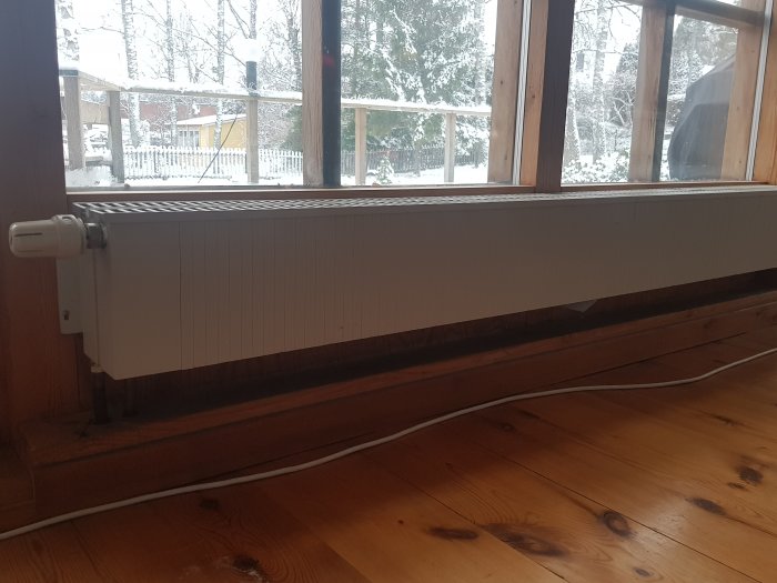 Vattenburen radiator under fönster i ett rum med utsikt över snötäckt trädgård.