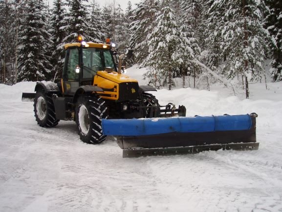 JCB 2150 Fast Track traktor med plog i snötäckt skogsmiljö, använd för att bereda väg för timmertransporter.