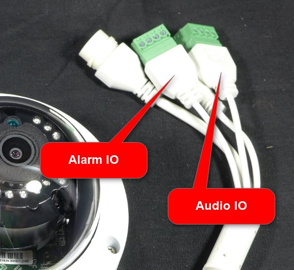 Hikvision-kamera med märkta Alarm IO och Audio IO anslutningar och vita kablar mot svart bakgrund.