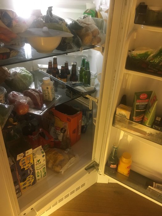 Öppet hörnkylskåp fullt med matvaror som visar en vardaglig och fullbelagd interiör.