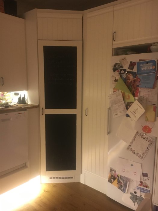 Norcool hörnkylskåp integrerat i ett stökigt kökshörn med anslagstavla täckt i notiser och bilder.