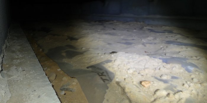 Plastfolie som inte sluter tätt mot balkarna med synligt grus och skräp ovanpå, i ett hus från 1992.