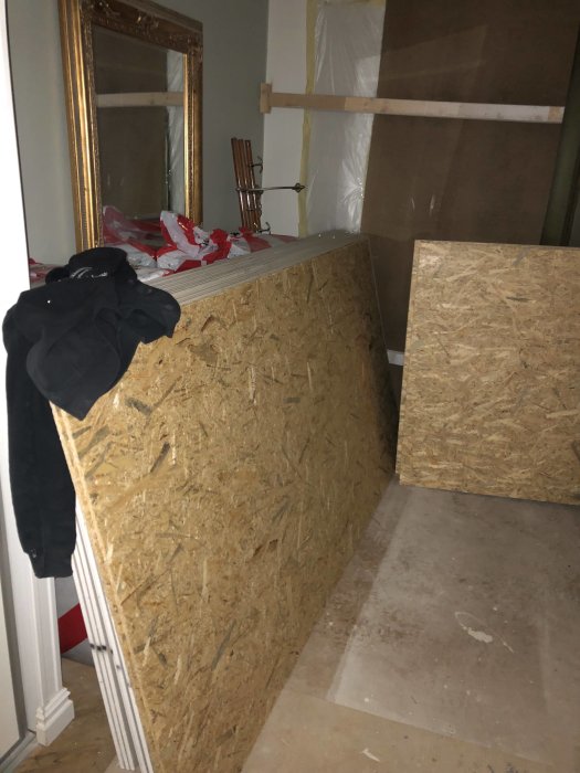 OSB-skivor står lutade mot en vägg i ett rum under renovering med byggmaterial synliga.