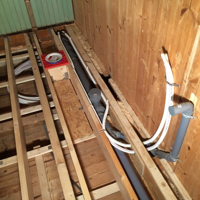 Installation av rör-i-rör och avloppsrör i öppet bjälklag för badrumsrenovering.