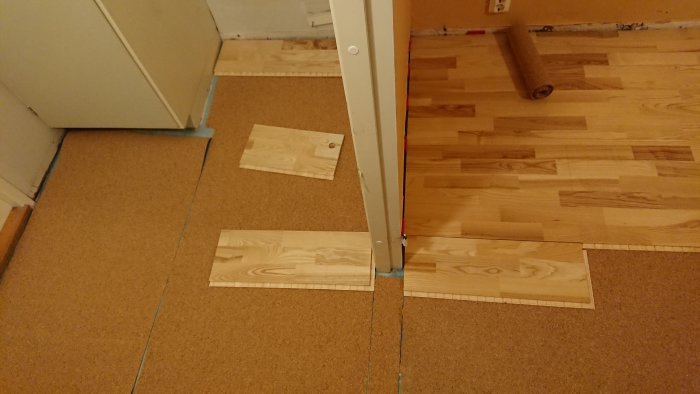 Ofullständig installation av laminatgolv vid tröskel med synlig korkmatta.
