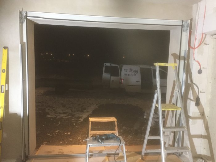 Garage under konstruktion med öppen port som visar en parkerad skåpbil utanför och en stege inuti.