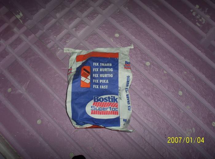 Säck med Bostik Fix Snabb ligger på ett nivellerat golv med rosa spårad frigolit för elvärmekabel.