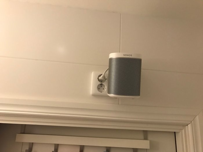 Sonos One högtalare monterad på vägg med kabel och väggfäste synligt.