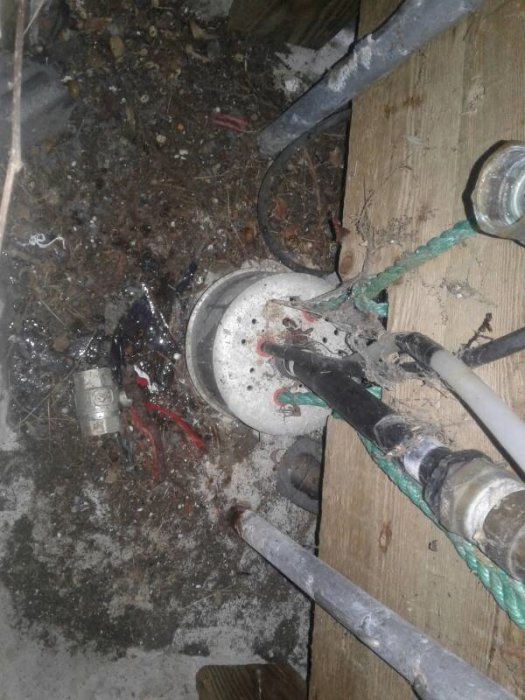 Brunnsutrustning med kablar, tryckvakt och flerledade rör i en smutsig och dammig installation.