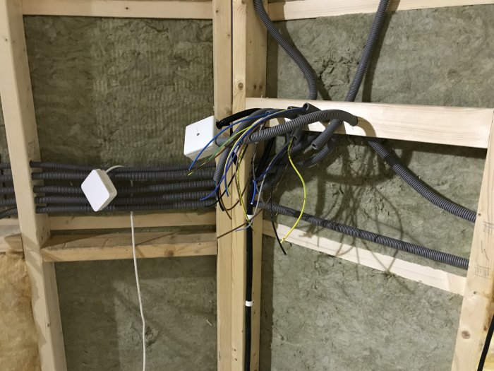 Elinstallation med flera dragna sladdar och slangar i en träregelkonstruktion med isolering, inför montering av central.