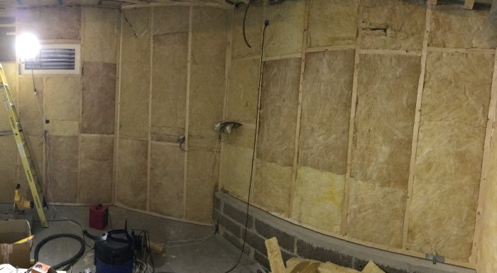 En verkstadsinredning med exponerad isolering och ramar för elinstallationer, inklusive sladdar och väggdosor.