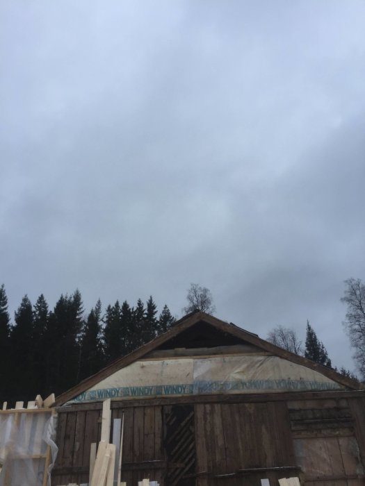 En halvfärdig byggnad med nedmonterade takstolar och träväggskonstruktion mot en molnig himmel.