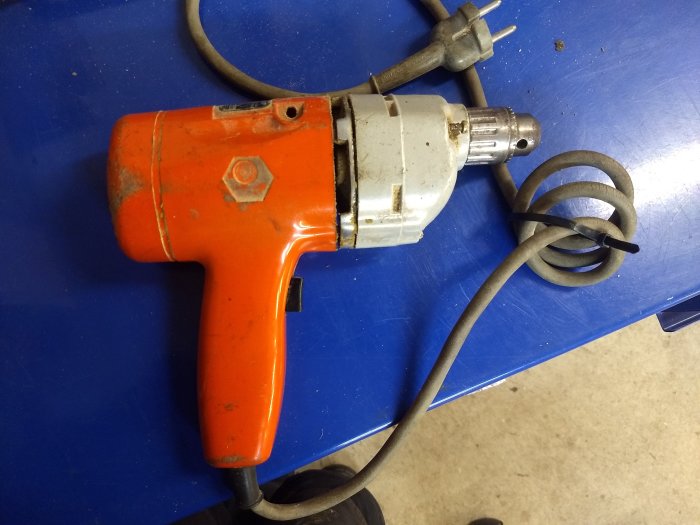 Gammal orange och silverfärgad Black & Decker borr med sladd på en blå arbetsyta.