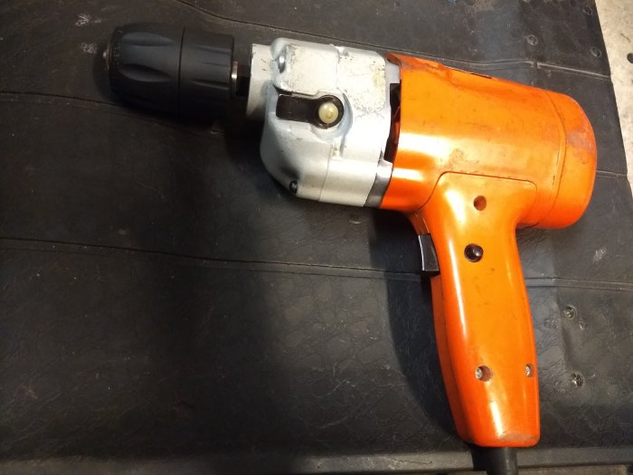 Orange och silverfärgad gammal Black & Decker borr med svart chuck ligger på en svart yta.