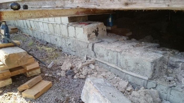 Husgrund som renoveras med nya betongblock, trästöttor och domkrafter för stöd under arbetet.