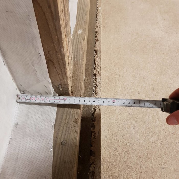 Måttband visar avstånd mellan träreglar och vägg vid isoleringsarbete i garage.