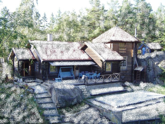 Ett trefasat trähus med ett nybyggt torn, omgivet av skog och en stenträdgård framför.