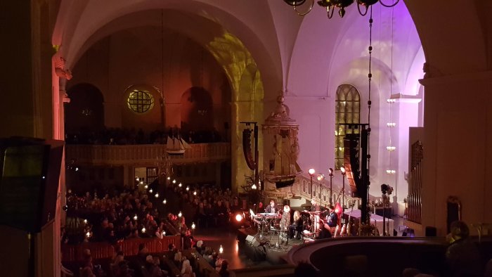 Konsert med publik i en kyrksal med färgad belysning och musiker på scenen.