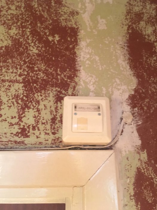 Gammalt telefonjack med sladd som löper över en dörrkarm mot en vit dosa.