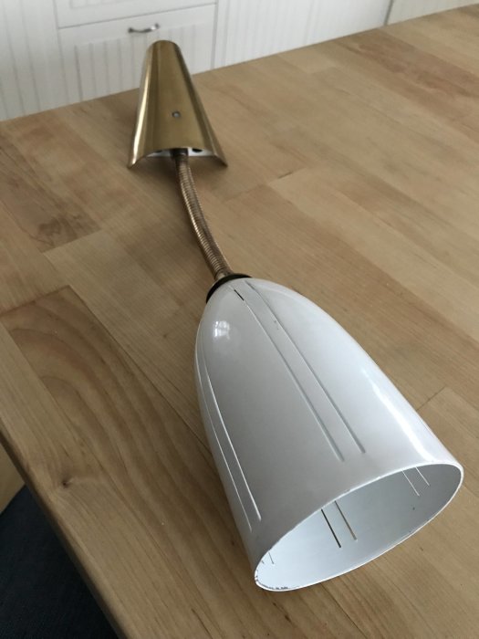 Retro sänglampa med böjbar arm och metallskärm placerad på ett träbord.