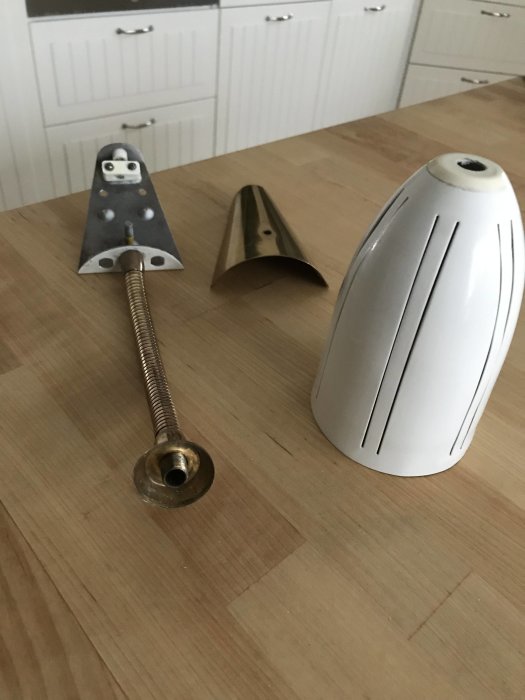 Retro sänglampa demonterad i delar med fäste, böjbar arm och skärm i metall på ett köksbord.