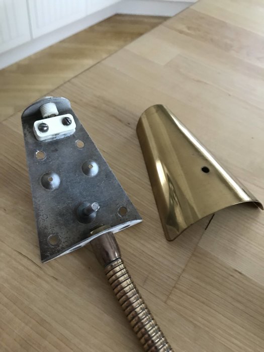 Avmonterad retrosänglampa med fäste och avtagen gyllene skärm placerade på trägolv.