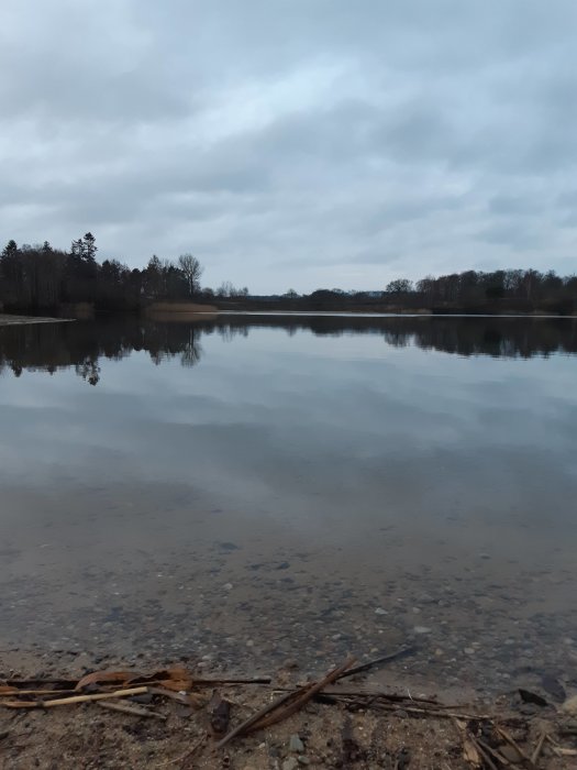 Stilla sjö med reflektion av molnig himmel, kallt väder, synlig vattentemperatur varmare än luften.