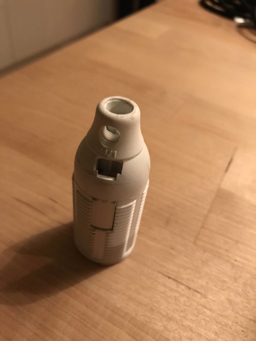 Gängad lamphållartopp placerad på ett bord, saknar den övre delen för att fästa en lampskärm.