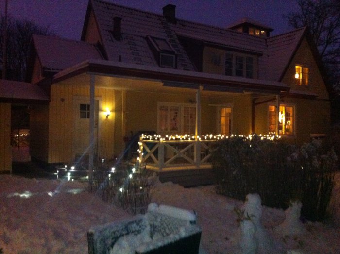 Hus i vinkelarkitektur med snötäckt tak och julbelysning i skymningen.