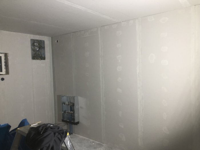 Interiör av ett garage under renovering med väggar som har dubbelgips och spacklade skarvar.