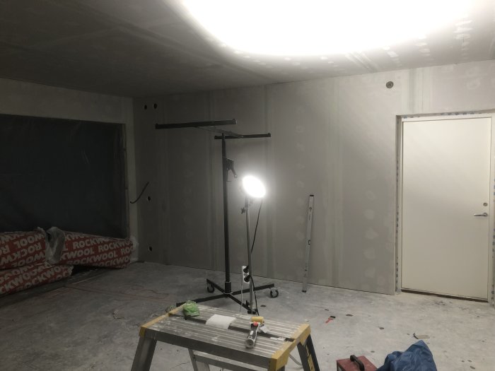 Inre bild av ett garage under renovering med dubbelgipsade väggar, spacklade skarvar och verktyg för byggjobbet.