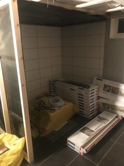 Halvfärdig bastu med reglar, bastufolie och väntande kakelpaket. Öppning för framtida glasvägg synlig.