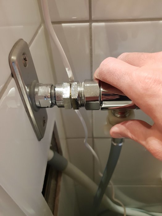 Hand som vrider på en kranfastsättning, mutter och grått gummi syns mot kakelvägg.