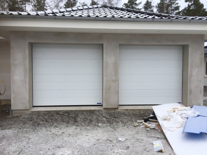 Två nya garageportar på ett hus med lite snö på taket och byggmaterial i förgrunden.