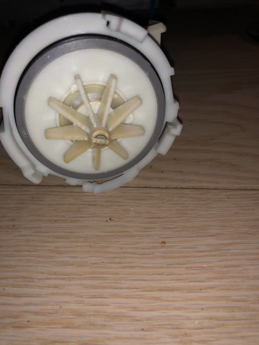 Närbild av en vit plastfläktventil mot träunderlag, eventuellt del av en byggprodukt.