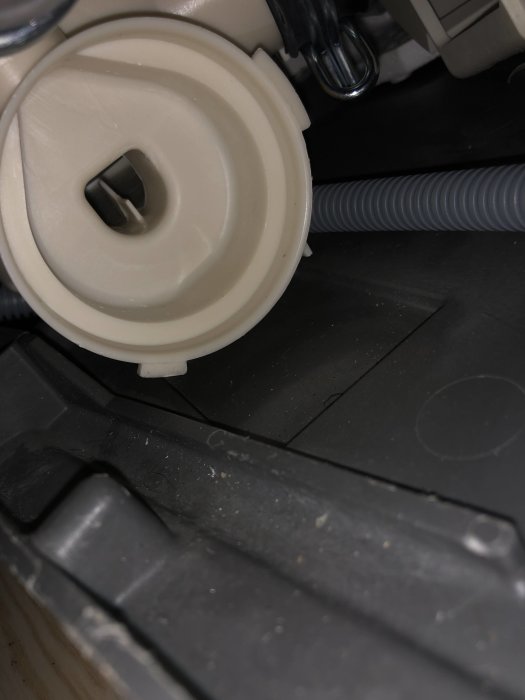 Närbild av en tvättmaskins avloppspump med synliga anslutningar och damm.