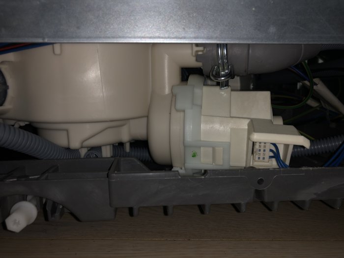 Installerad motor i en vit apparat, synlig med kablar och slangar under en bänk.