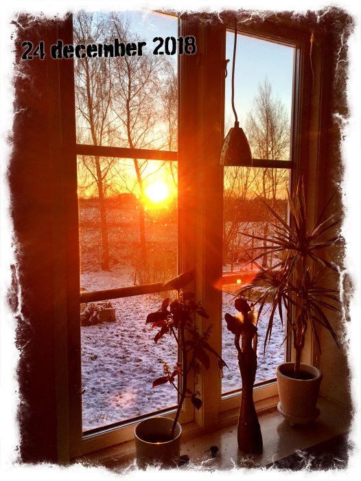 Solnedgång sett genom ett snötäckt fönster med datumet 24 december 2018.