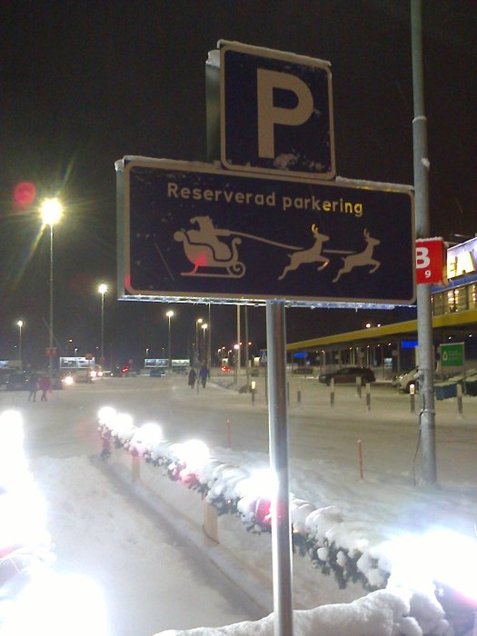 Parkeringskylt med snö och juldekoration av släde och renar, antyder reserverad plats för tomten.