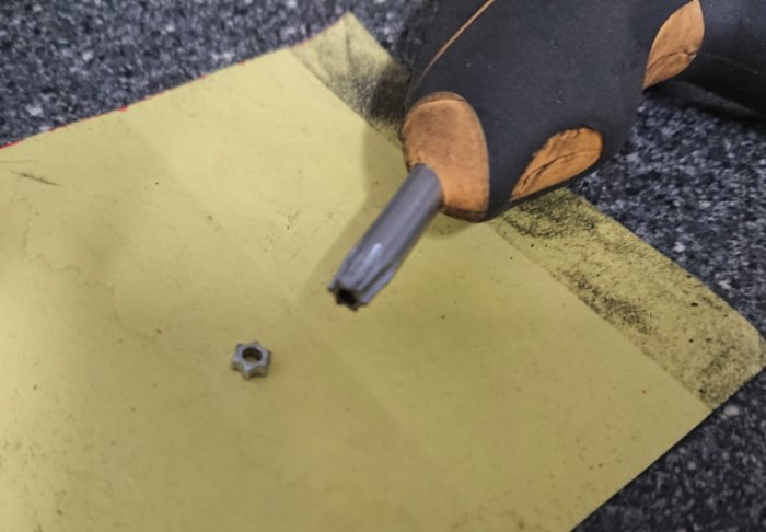 Torxnyckel med brutet huvud och en säkerhetstorksskruv på en gul yta.