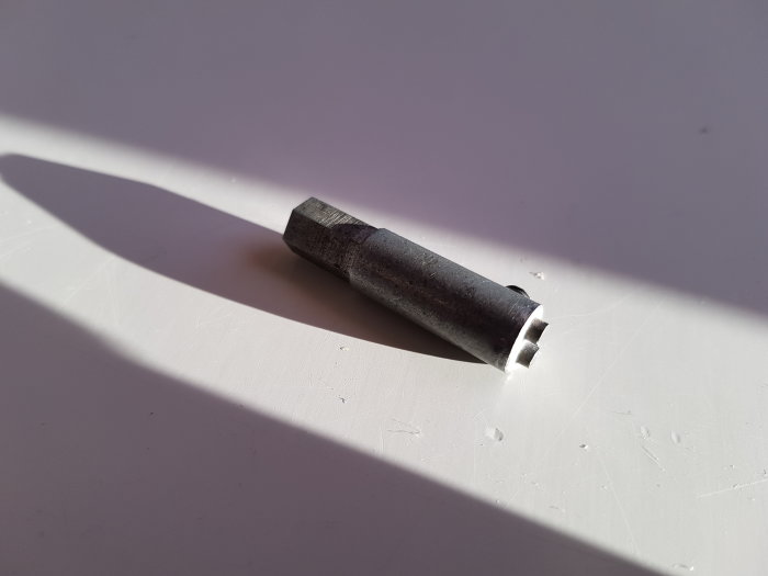 En genomtänkt bild av en metallisk expanderspik som ligger på en vit yta med en tydlig skugga.