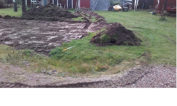 Uppgrävd mark med högar av jord på en tomt, början av ett verkstadsbyggprojekt på landsbygden.
