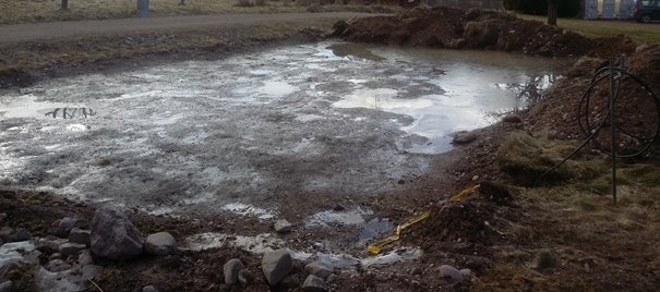 Grundarbete för byggprojekt med grävt område, vattenansamlingar och rullad el-kabel ute på landet.