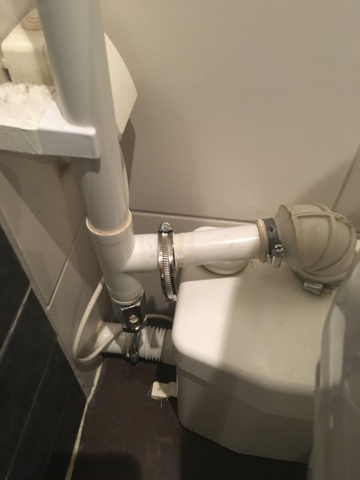 Makeshift repair of white plumbing pipes using electrical tape and a hose clamp next to a bathroom fixture.