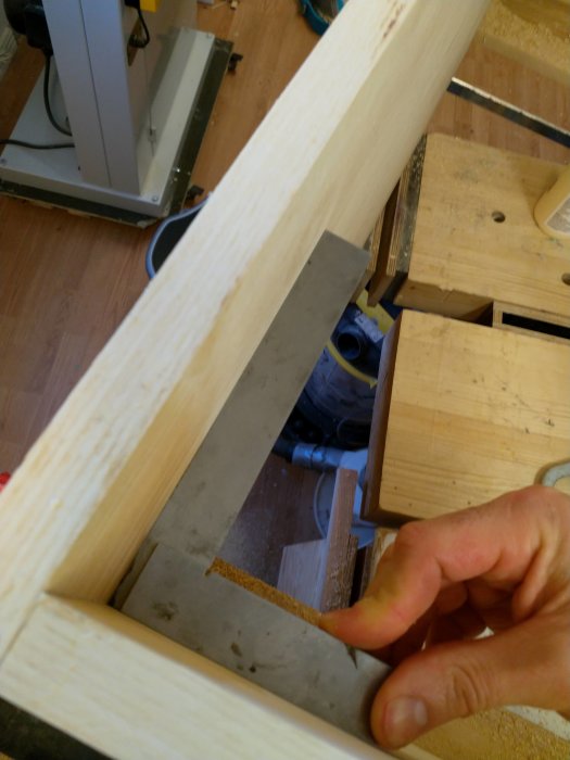 Del av träskåpskonstruktion med regel och spår för baksida, verktyg och arbetsmaterial i bakgrunden.