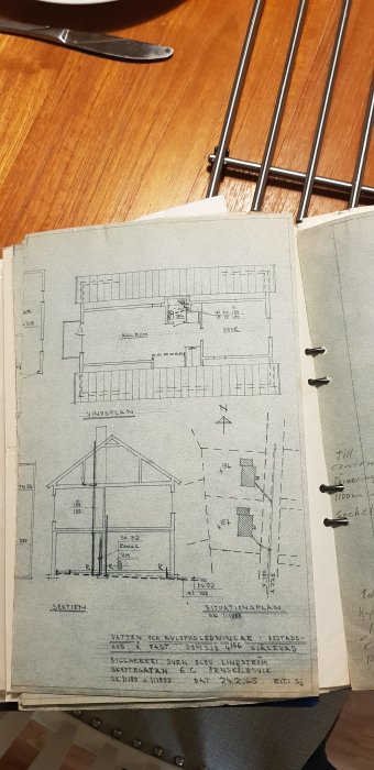 Arkitektritning av ett hus med planlösning och sektion visas på ett bord med anteckningar och skisser i marginalerna.