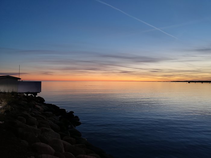 Solnedgång över Kalmar sund med långsträckta moln och stenbelagd kustlinje.