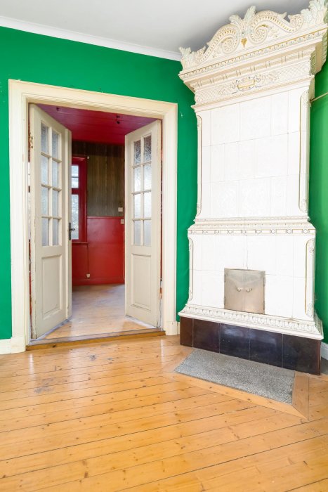 Historiskt rum med dekorativ kakelugn, trägolv och färgglada väggar.